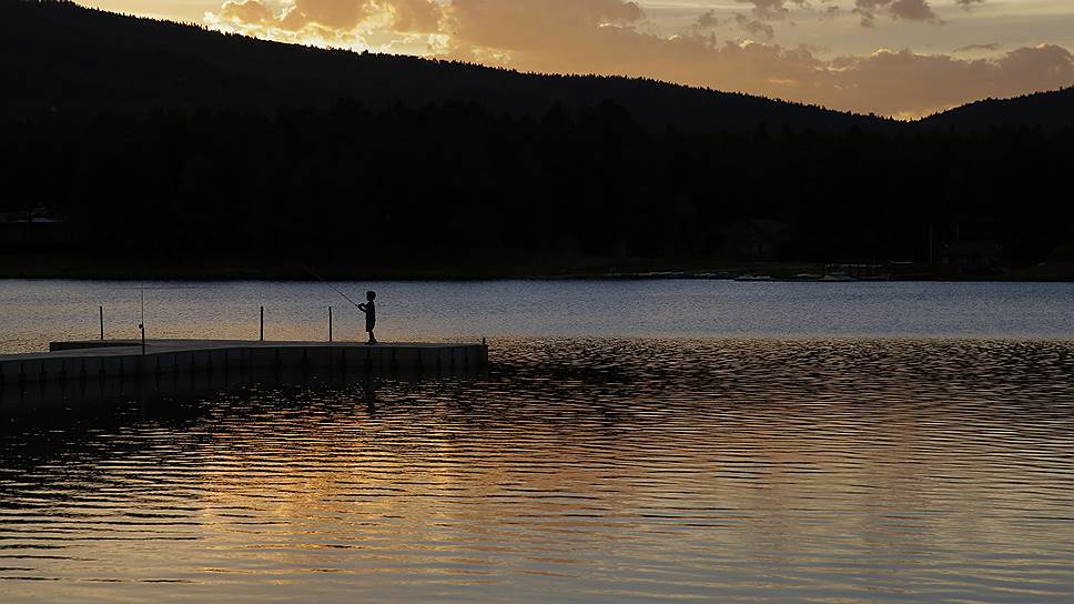 Фейр-Анджел, США. Мальчик рыбачит на закате на озере Монтеверде 