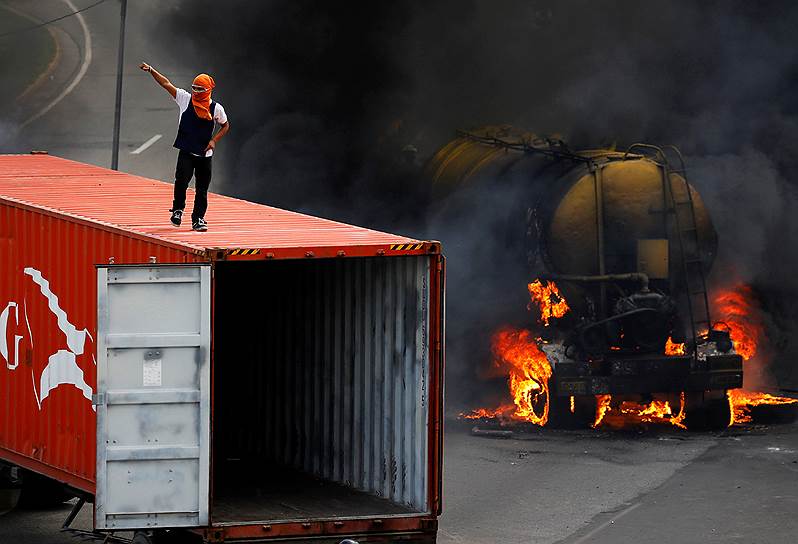 Каракас, Венесуэла. Участник антиправительственных протестов на крыше грузовика на фоне горящих автомобилей 
