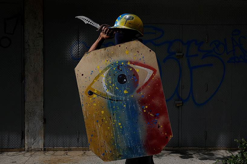 Каракас, Венесуэла. Участник антиправительственной демонстрации с щитом и мечом готовится идти на акцию
