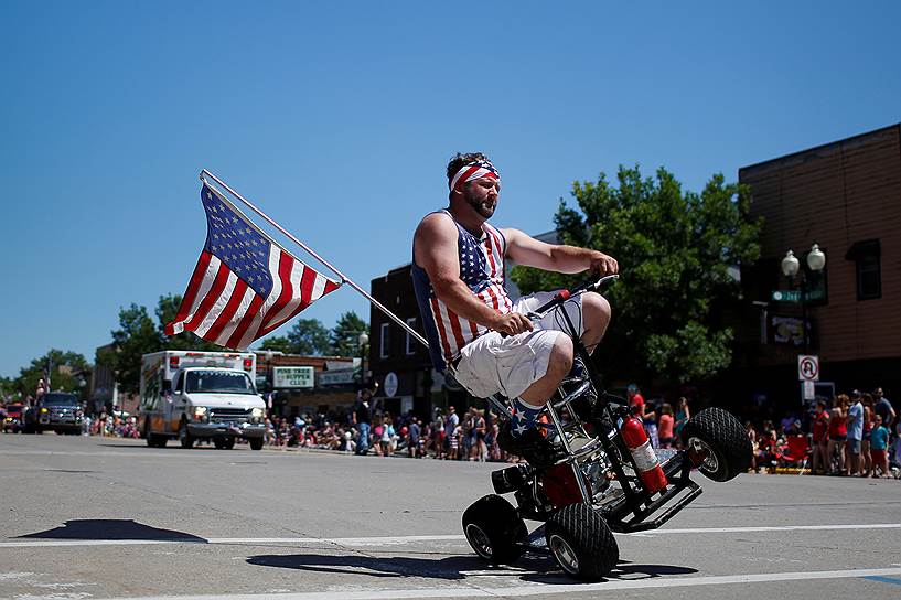 Томагавк, штат Висконсин. Участник парада совершает трюки на квадроцикле, разукрашенном в символику США 