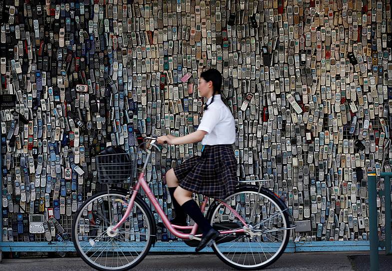 Токио, Япония. Девушка проезжает мимо стены магазина электроники, украшенной старыми сотовыми телефонами