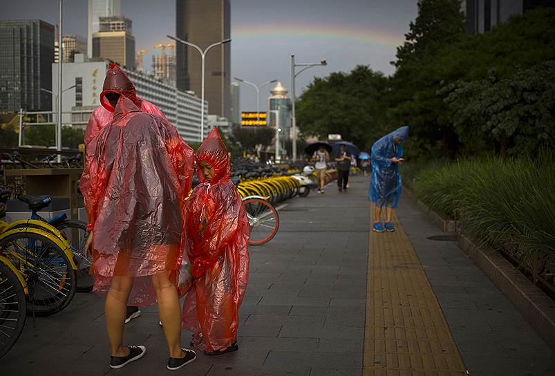 Пекин, Китай. Одетые в дождевики люди на фоне радуги