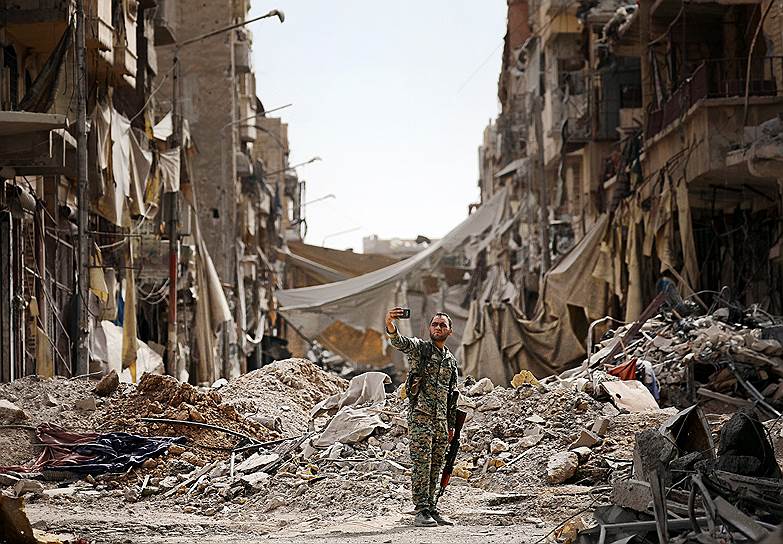 Ракка, Сирия. Боец &quot;Сирийских демократических сил&quot; делает селфи на фоне разрушенных домов