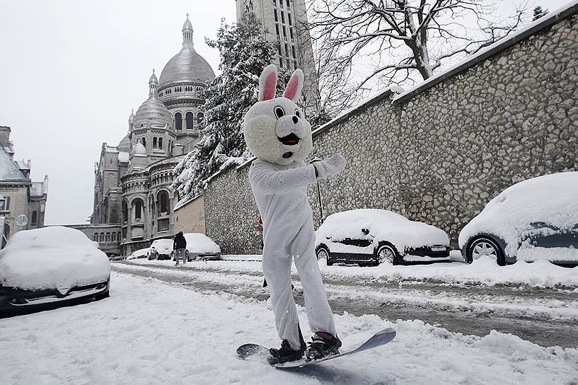 Париж, Франция. Местный житель в костюме кролика катается на сноуборде на Монмартре