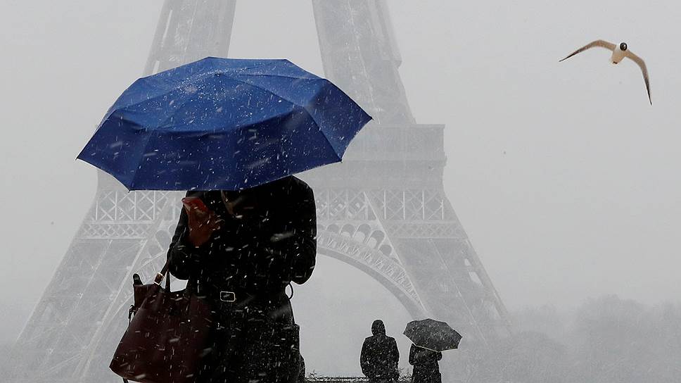 Париж, Франция. Местная жительница прогуливается под зонтом рядом с Эйфелевой башней 