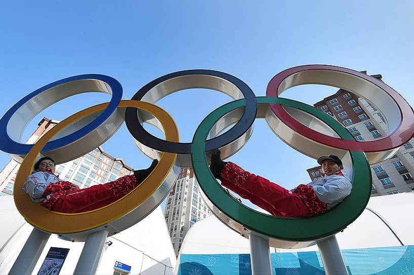 Спортсмены фотографируются на фоне стеллы с пятью олимпийским кольцами в Олимпийской деревне
