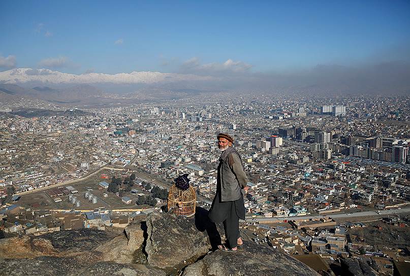 Кабул, Афганистан. Местный житель с клеткой для птицы стоит на холме 