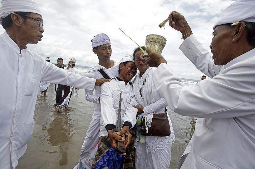 Бали, Индонезия.  Индуистский священник окропляет святой водой местного жителя во время религиозного ритуала 