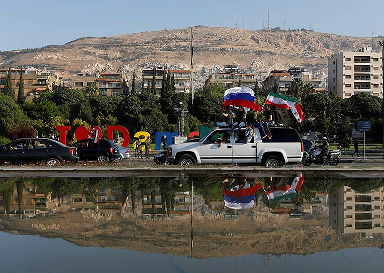 Сирийцы с российскими и сирийскими флагами во время акции протеста против авиаударов США в Дамаске