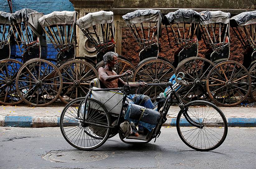Калькутта, Индия. Инвалид передвигается на трехколесной коляске вдоль припаркованных повозок-рикш