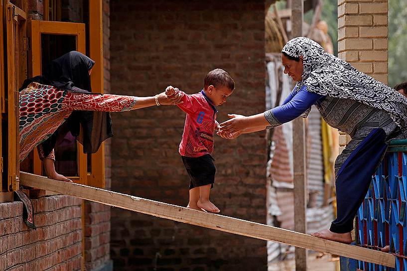Сринагар, Индия. Женщины помогают ребенку перебраться в другой дом после ливневого паводка в районе Тейлбал