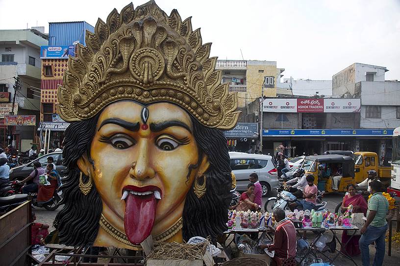 Хайдарабад, Индия. Местные жители покупают на рынке статуэтки богини Лакшми на фоне большого изображения богини Кали