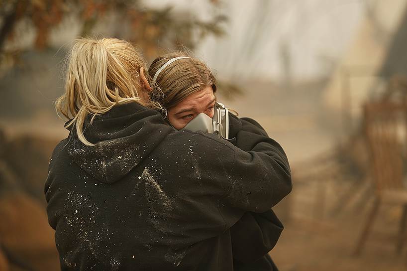 Местная жительница Кристин Харви (слева) утешает свою дочь Арайю у остатков их сгоревшего дома