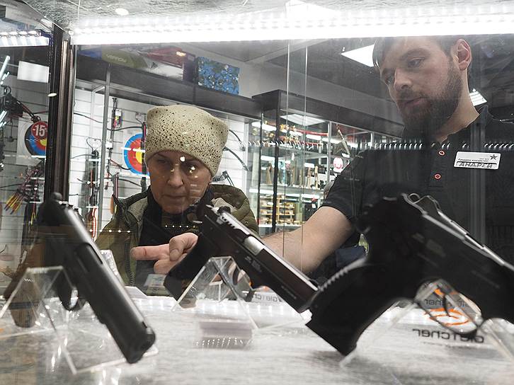 Москва, Россия. Покупательница перед витриной с пистолетами в магазине «Солдат удачи»
