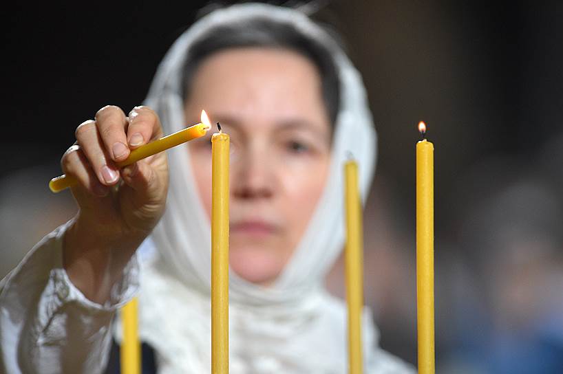 Верующая зажигает церковные свечи во время богослужения