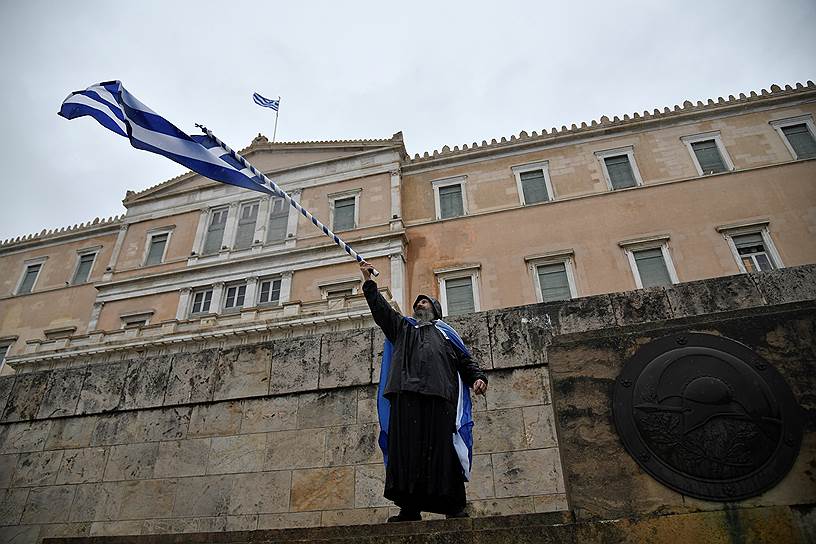 Монах держит греческий флаг во время акции протеста в день ратификации соглашения греческим парламентом. Митинг противников соглашения о переименовании Македонии начался 20 января 