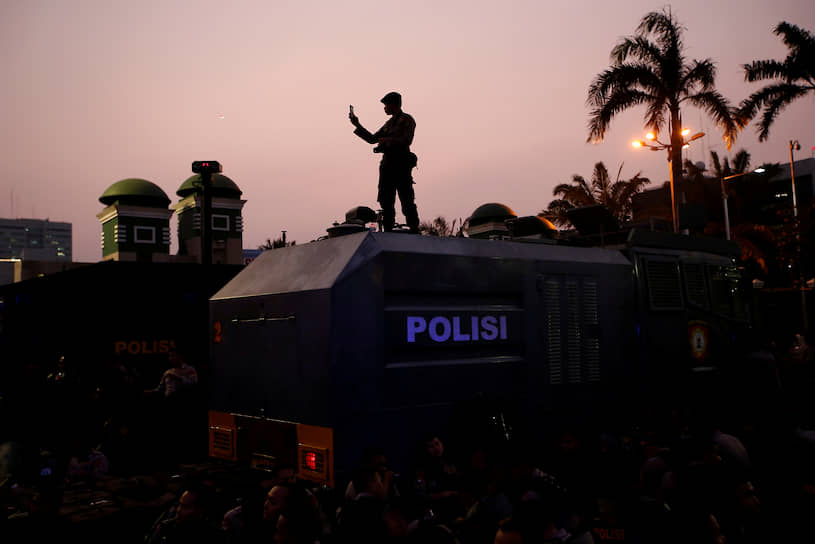 Джакарта, Индонезия. Полицейский держит в руках телефон во время акции протеста студентов у здания парламента