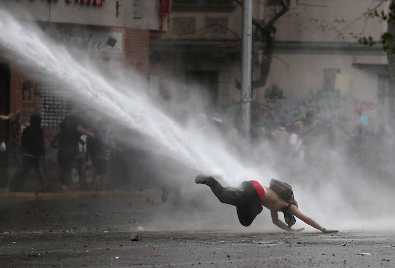 Сантьяго, Чили. Участник антиправительственной акции протеста, сбитый с ног струей из водомета