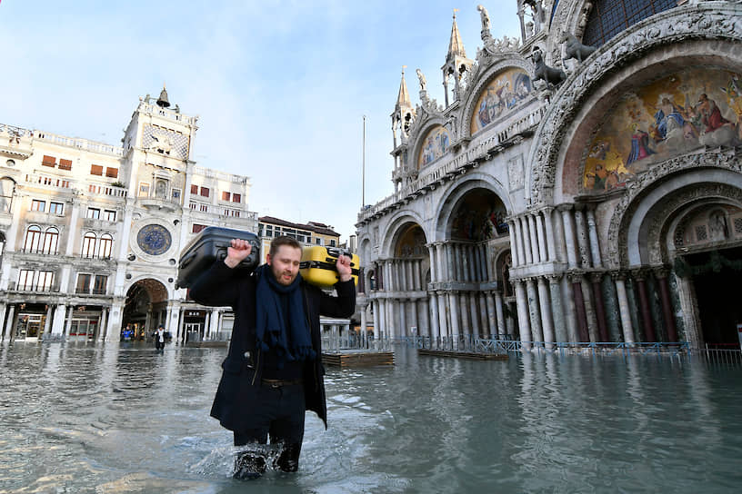 Венеция, Италия. Мужчина несет чемоданы по затопленной площади Святого Петра