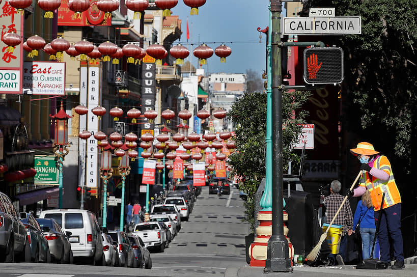 Уборщик в маске подметают улицу в районе Чайна-таун в Сан-Франциско, США
