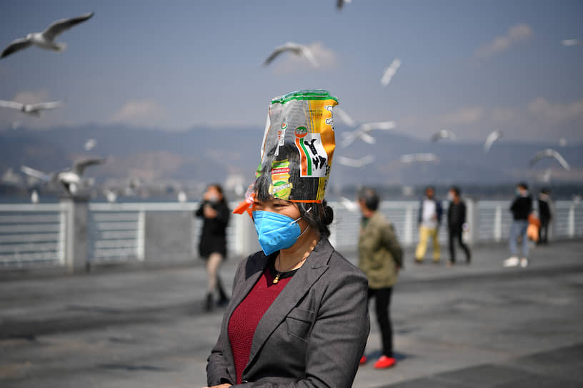 Провинция Юньнань, Китай. Женщина в маске с пакетом на голове для защиты от коронавируса
