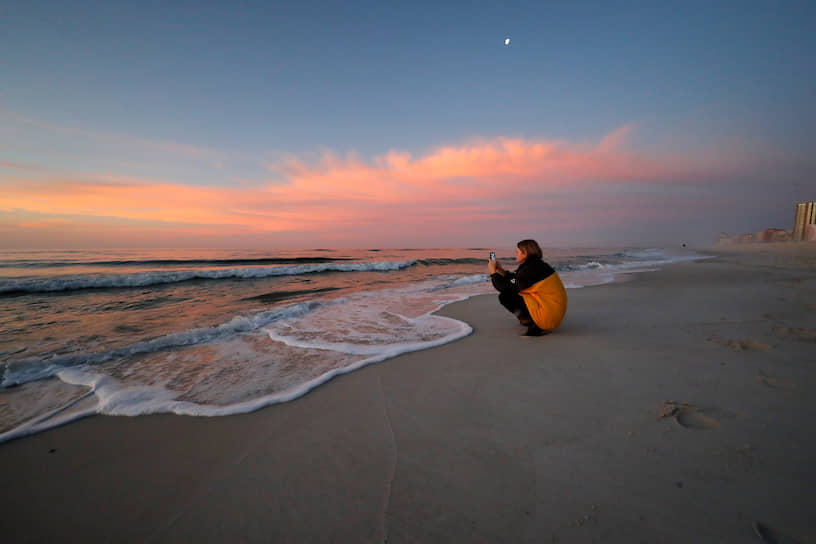 Орандж-Бич, штат Алабама, США. Девушка фотографирует закат на городском пляже 