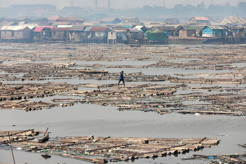 Лагос, Нигерия. Мужчина переходит реку по бревнам