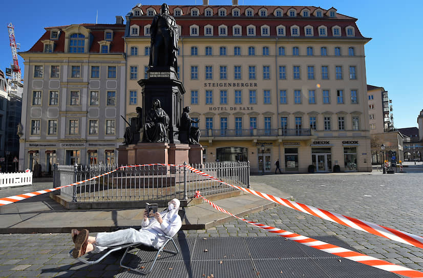 Дрезден, Германия. Мужчина в защитном костюме и маске читает книгу