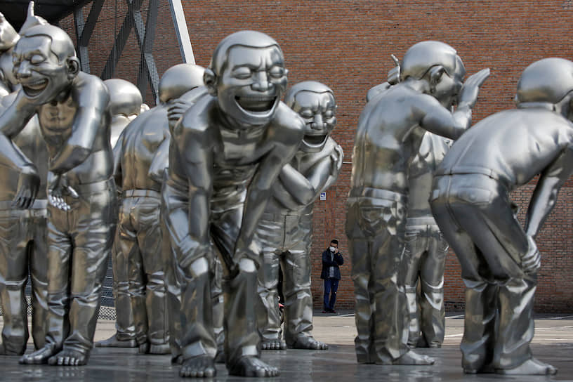 Пекин, Китай. Мужчина в медицинской маске стоит около группы скульптур