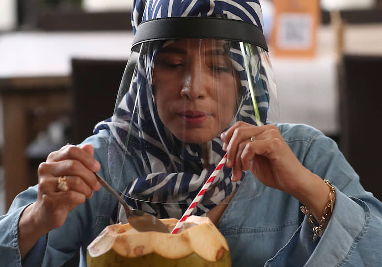 Джакарта, Индонезия. Женщина в защитной маске ест кокос