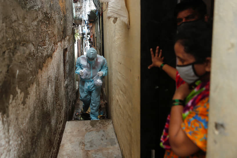 Мумбаи, Индия. Врач в защитном костюме идет измерять температуру у жителей трущоб
