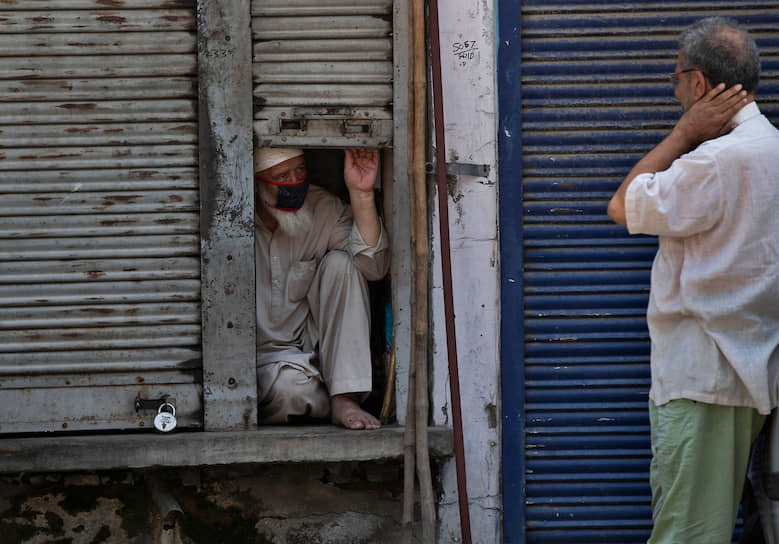 Сринагар, Индия. Продавец закрытого на карантин магазина разговаривает с мужчиной 
