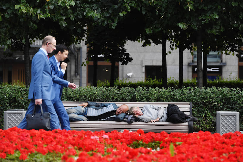 Москва, Россия. Мужчины в деловых костюмах проходят мимо лавочки со спящими людьми