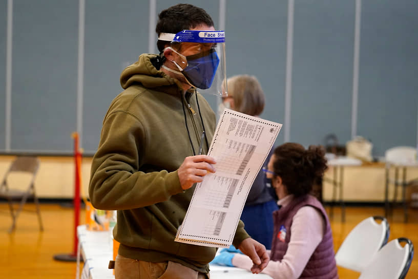 Избиратель в двух масках и защитном экране голосует на избирательном участке в Портленде