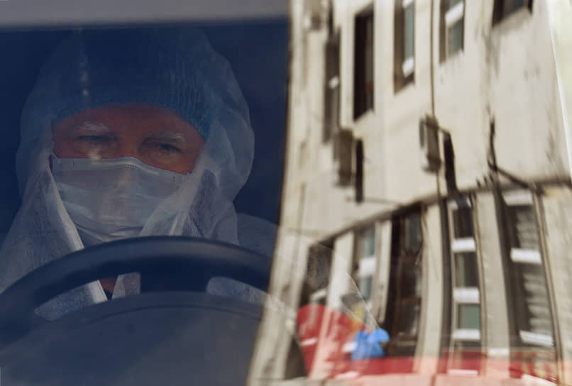 Водитель в защитном костюме и медицинской маске за рулем машины скорой помощи