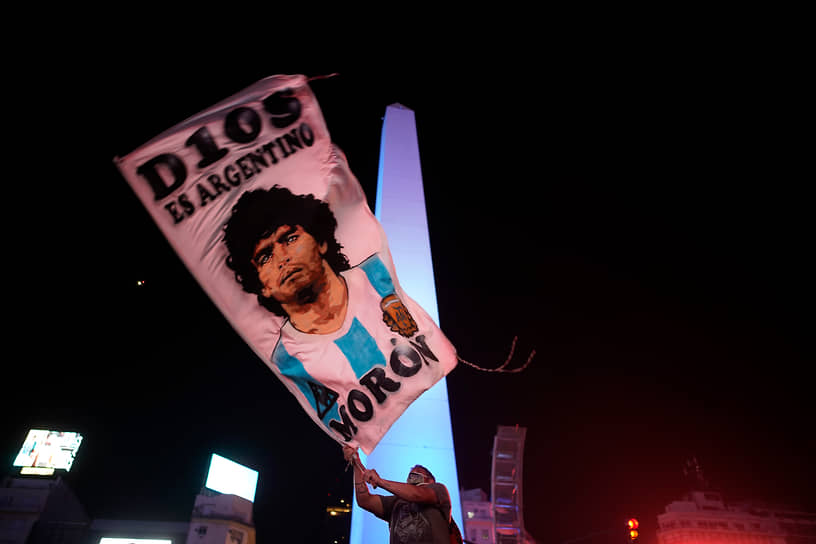 Мужчина размахивает флагом, на котором изображен Диего Марадона, в центре Буэнос-Айреса 