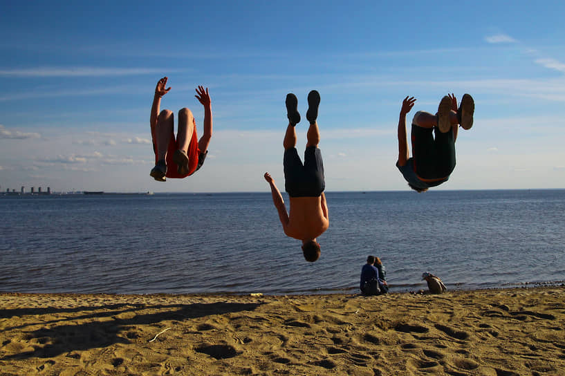 Молодые люди прыгают на берегу моря в парке имени 300-летия Санкт-Петербурга