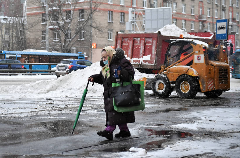Женщина идет по улице во время уборки снега 