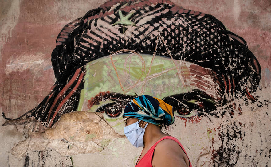 Гавана, Куба. Женщина в медицинской маске идет мимо полуразрушенного граффити с портретом Эрнесто Че Гевары