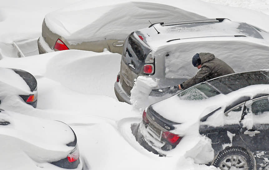 Водитель чистит автомобиль от снега