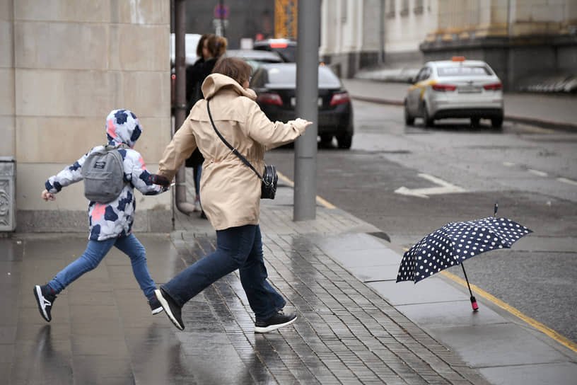 Москва, Россия. Женщина бежит с ребенком за улетевшим зонтом