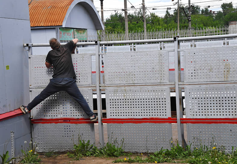 Москва, Россия. Мужчина лезет через ограждение железнодорожной станции