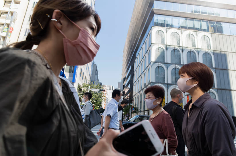 Токио, Япония. Люди в масках идут по пешеходному переходу