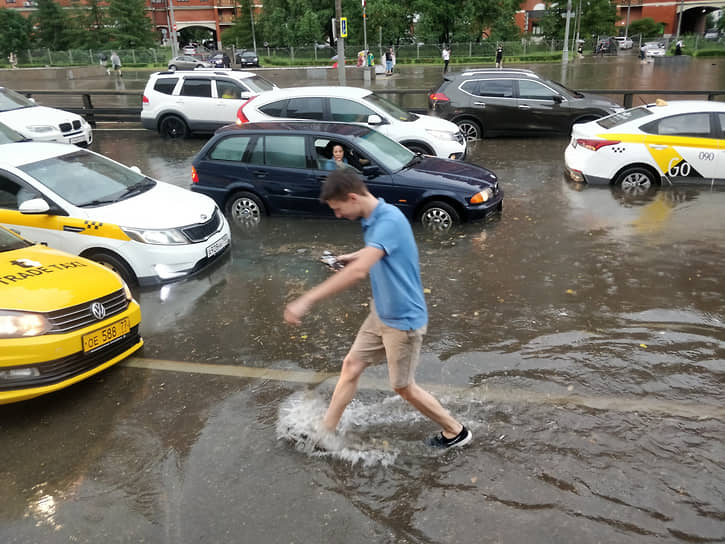Молодой человек пытается перейти через затопленную дорогу 