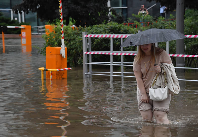 Женщина переходит затопленную из-за сильного дождя дорогу