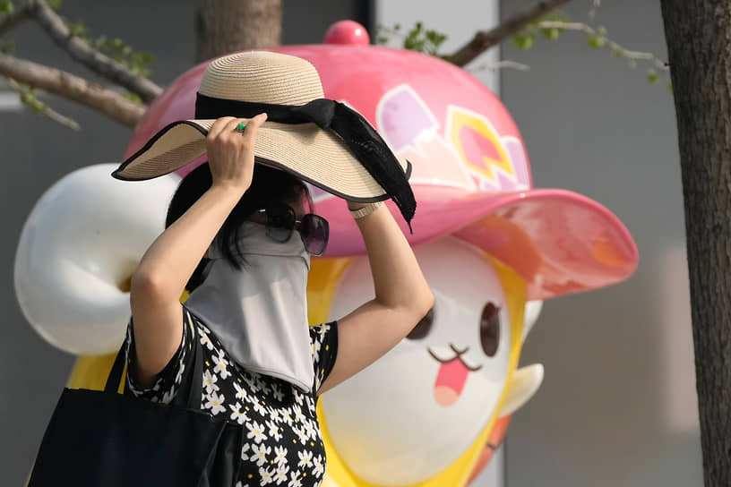 Пекин, Китай. Женщина в маске идет мимо фигуры мултипликационного персонажа 