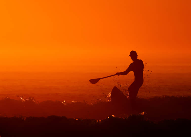 Пломёр, Франция. Мужчина на доске для серфинга на фоне заката 
