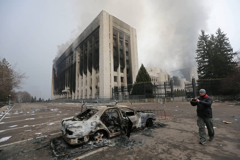 Мужчина фотографирует сожженный в ходе протестов в Алматы автомобиль 