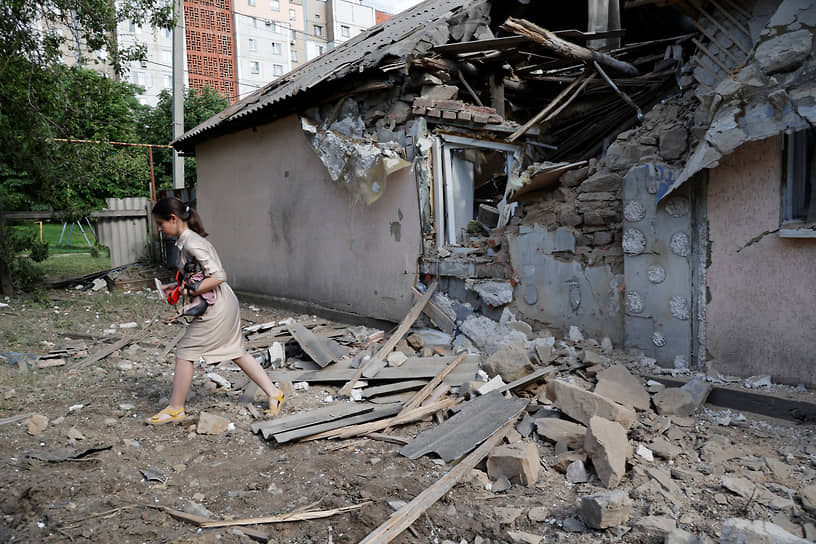 Жительница Донецка с собакой проходит мимо разрушенного дома
