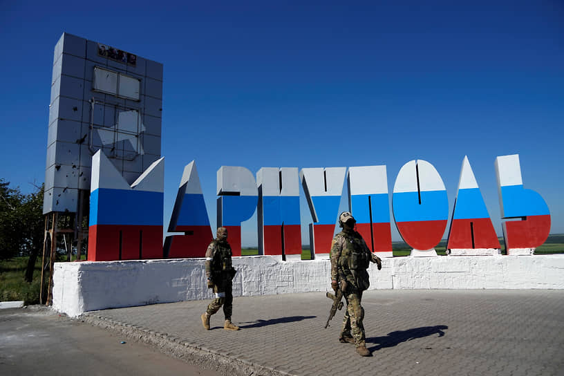 Военнослужащие проходят мимо перекрашенного в цвета российского флага названия города на въезде в Мариуполь